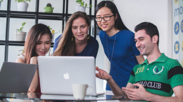 Group of four colleagues collaborating around a laptop, smiling and engaged in discussion